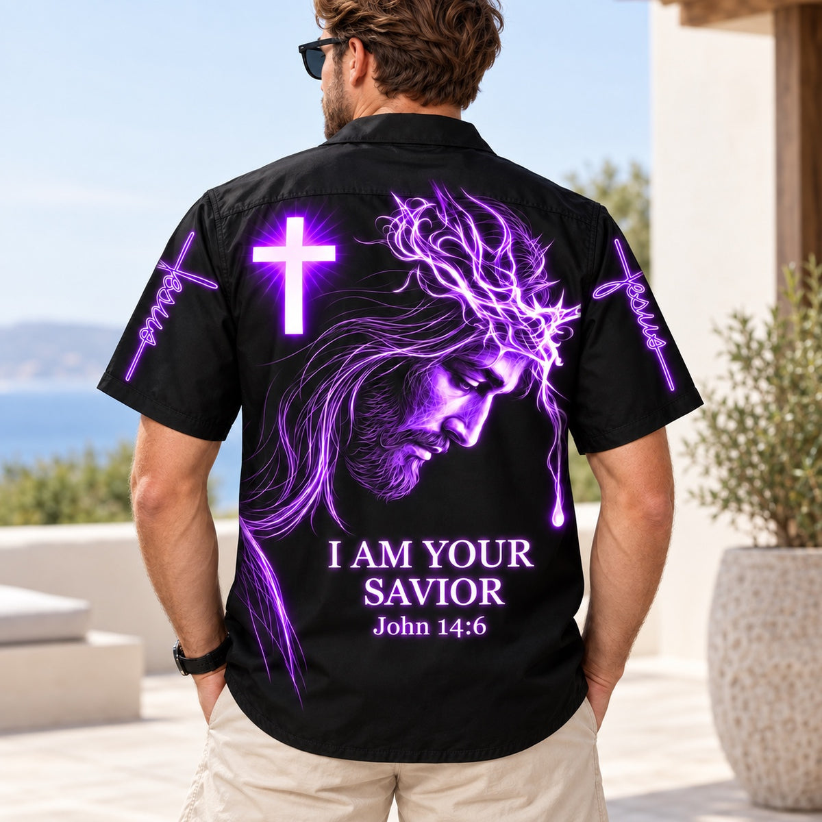 Man wearing the black I Am Your Savior Hawaiian shirt on a seaside terrace, back print view