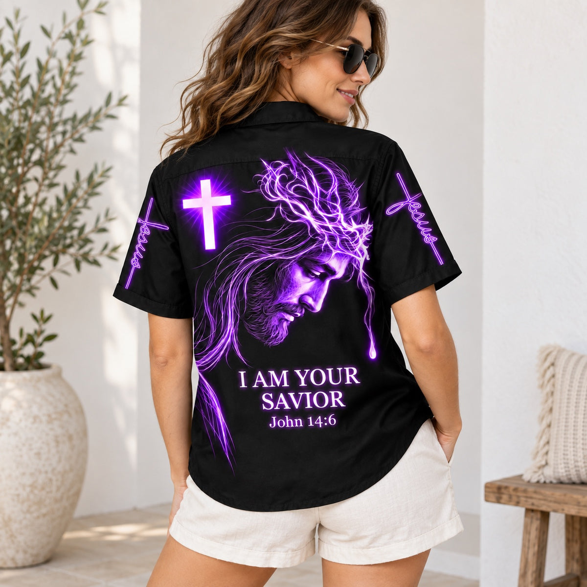 Woman wearing the black I Am Your Savior Hawaiian shirt with a purple neon Jesus portrait, glowing cross and John 14:6 on the back