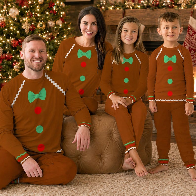 Family of four wearing matching gingerbread cookie Christmas pajamas by the fireplace
