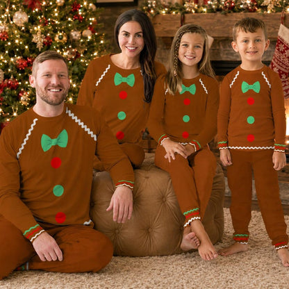 Family of four wearing matching gingerbread cookie Christmas pajamas by the fireplace