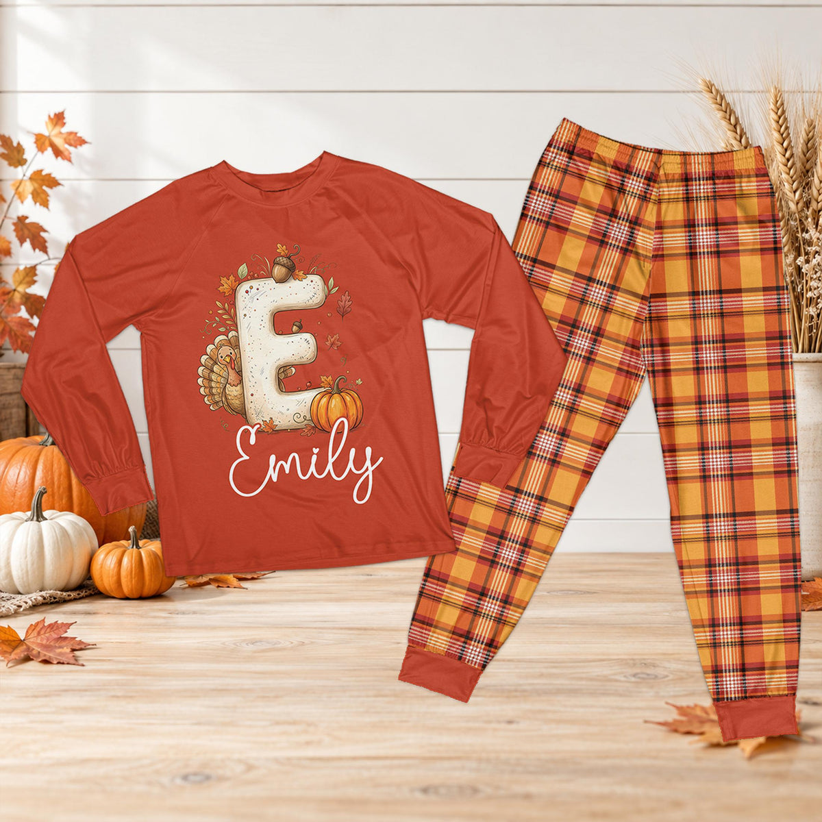Personalized thanksgiving pajama set featuring an orange top with custom name, turkey and fall leaves design, and matching plaid pants, front view