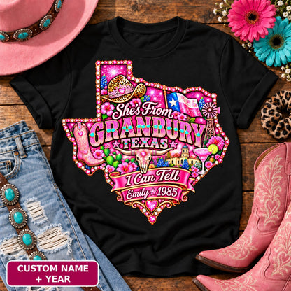 Personalized She's From Granbury Texas I Can Tell t-shirt on Black, custom name and year badge, pink glitter Texas with rhinestone border, leopard cowgirl hat, flag, boots, longhorn and custom name and year banner NEW2